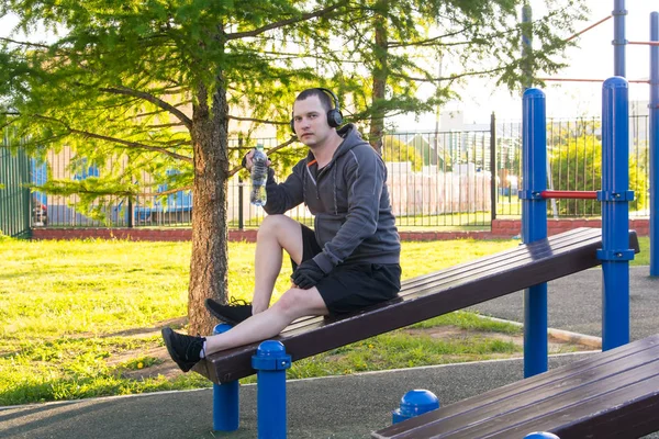 スポーツのアプローチの間隔の間に 男は水のボトルを保持し シミュレータに座って 屋外で音楽を聞きます — ストック写真