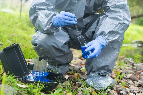 Koruyucu giysi ve mavi lastik eldiven konusunda uzman biri su analizi için mavi bir reaktör ve yakın plan bir pipet kullanıyor.
