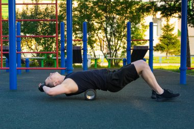 Sporcu, açık hava spor sahasında masaj silindiriyle geri dönüyor.