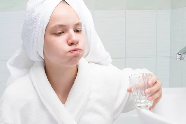 girl rinses her mouth in the morning with clean water from a glass