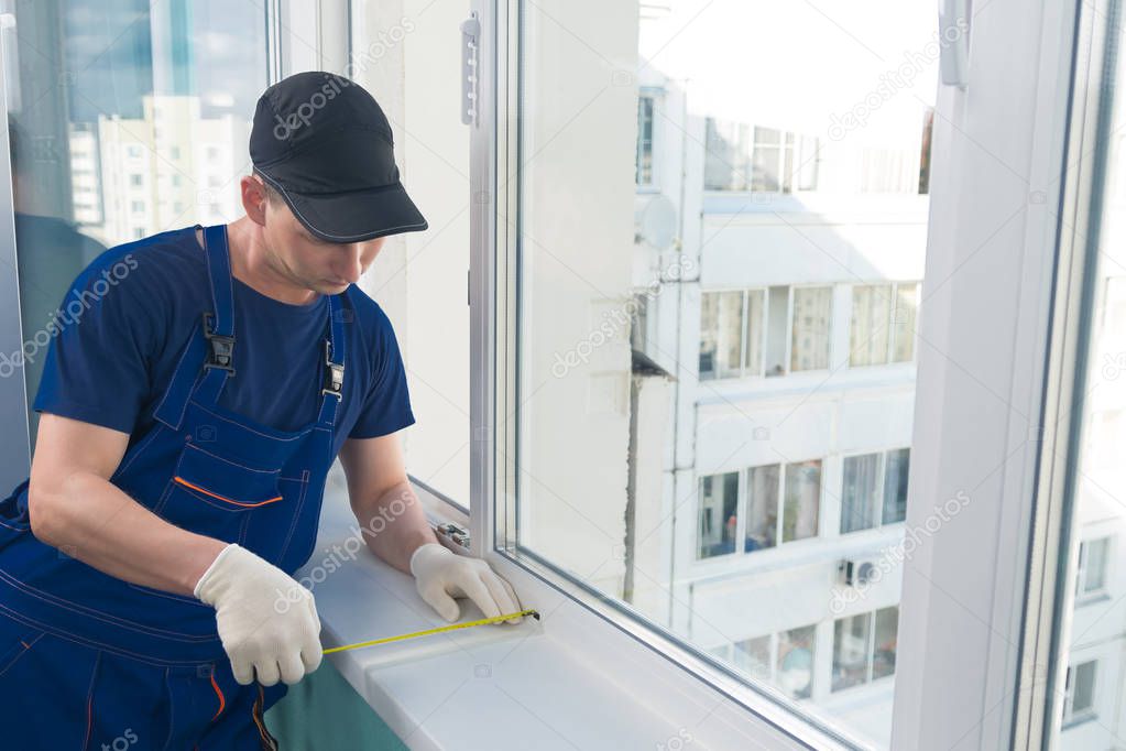 worker in blue uniform, measures the width of the windowsill with a yellow meter