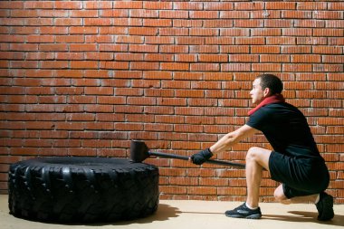 Spor yapan bir adam, tuğla bir duvarın arkasında siyah kauçuğa demir bir motol ile vurur.