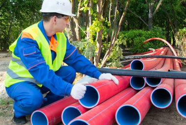 Beyaz miğferli bir müteahhit, üst üste yığılmış kırmızı plastik borular çıkarıyor, yazıtlar için bir yer var.