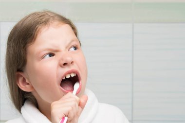 Kız dişlerini fırçalıyor, ağzını ardına kadar açıyor, yakın plan, yazıtlar için bir yer var.