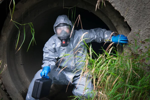 scientist in protective clothing, with a suitcase out of the drain pipe, which took a sample for testing, close-up