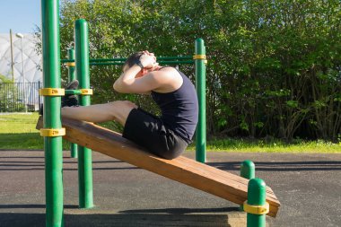 Adam parkta eğimli bir bankta kas egzersizi yapıyor.