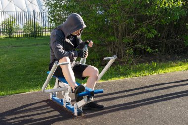 Kapüşonlu bir adam simülatörde spor yaptıktan sonra suyu açar.