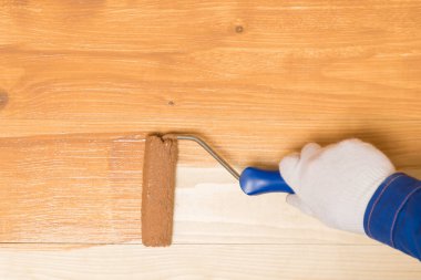 Boya silindirli bir el, ahşap bir yüzeyi koyu cila ile boyar. Üstünde yazı için bir yer vardır.