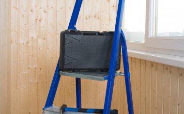 Odanın onarımı için gerekli aletlerin olduğu kara kutu, merdivenlerde duruyor, ahşap bir duvarın arkasında.