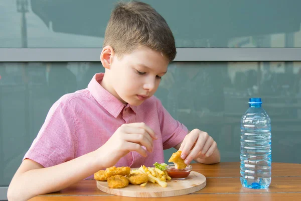 テーブルに座っている男の子はファーストフードを食べ ナゲットはソースを食べ — ストック写真