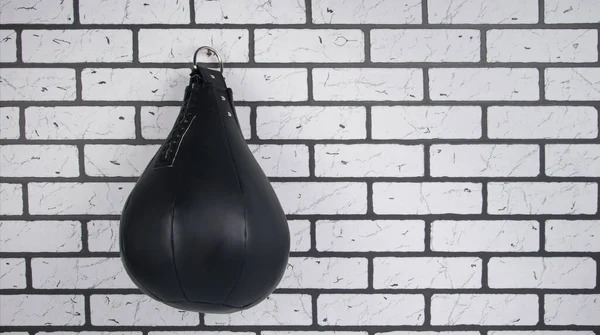 a Boxing bag, hanging on a hook , against a white brick wall, there is a place for the inscription