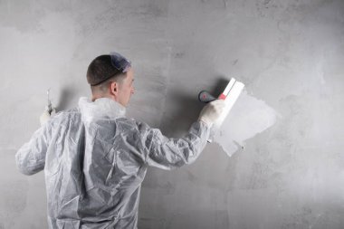 Usta büyük bir spatulayla beton duvarı yıkmaya çalışıyor, beyaz bir solüsyon uyguluyor.