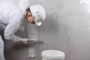 Beyaz başlıklı usta prizlerin altına elektrik kabloları yerleştirmek için ara verdi. Sağda yazıtlar için bir yer var.