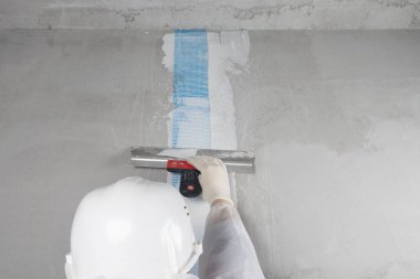 Beyaz kasklı bir tamirci, duvardaki dikişe, dikiz aynasına, yakın plana spatulayla spatula yapıştırır.