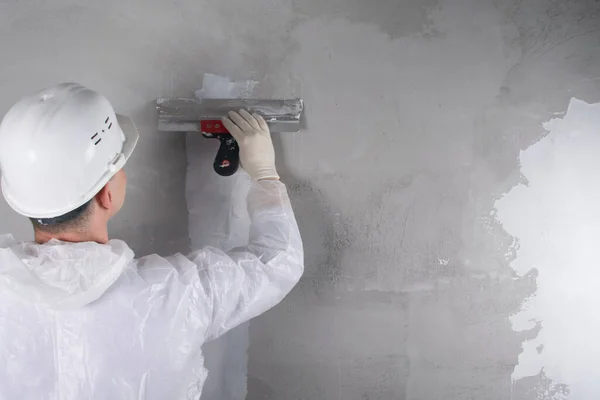 master in protective uniform and hard hat, closes a crack in the wall with a white mixture, there is a place for the inscription, rear view