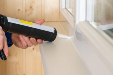 Bir adam beyaz silikon ve özel bir aletle plastik pencerelerin çatlaklarını kapatır.