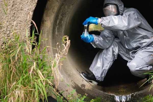 a man in a protective suit and mask in a large sewer took a sample of water for analysis