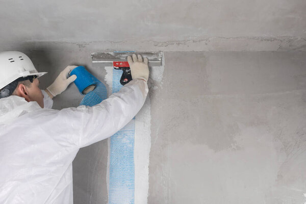 worker in hard hat repairs walls indoors, back view