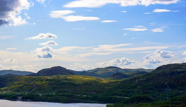 Blue sky over the hills in the Murmansk region. The low Northern sky breaks through the rays of the sun, reflected from the trees and bushes. Murmansk region, near Teriberka. Russi