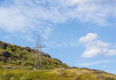 Yeşillikler ile çevrili bir dağda yalnız bir elektrik demir direği. Kablolu elektrik enerjinin en çevre dostu türüdür. Fotoğrafta tepe gökyüzü ile çapraz yatıyor