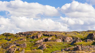 Alçak Kuzey gökyüzüne karşı çimenlerde doğranmış büyük kayalar. Kabarık beyaz bulutlar kayalar, tepeler ve otlar üzerinde sorunsuz hareket