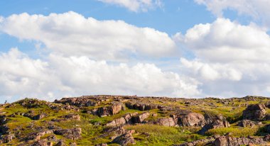 Alçak Kuzey gökyüzüne karşı çimenlerde doğranmış büyük kayalar. Kabarık beyaz bulutlar kayalar, tepeler ve otlar üzerinde sorunsuz hareket