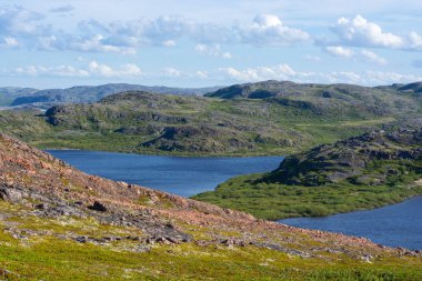 Güzel engebeli manzara. Kabarık bulutlar antik tepelerin üzerinden uçar, tepeler masmavi su yüzeyini keser. Bu yerlerde huzurlu ve sakin bir ruh hali hüküm sürüyor. Murmansk region, Rusya Federasyonu
