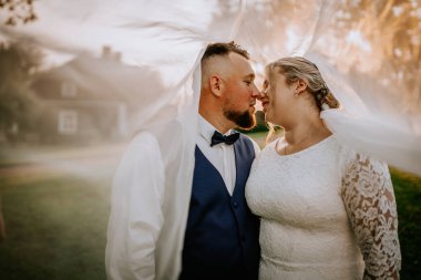 Bride and groom share an intimate moment under the brides flowing veil during golden hour, standing close and smiling lovingly at each other