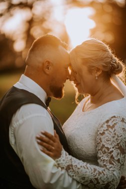 A bride and groom share an intimate moment at sunset, their foreheads touching as they smile, glowing in the warm golden light of their wedding day.
