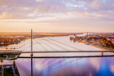 Riga, Letonya - 14 Nisan 2014 - Letonya Riga, Letonya 'daki Daugava Nehri' ni kapsayan Vansu Köprüsü 'nün hava görüntüsü, renkli bir günbatımında yansımaları ve uzaklıktaki sanayi silueti.