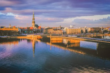 Riga, Letonya - 14 Nisan 2014 - Taştan Köprü, Daugava Nehri ve St. Peters Kilisesi 'nin ikonik kulesinin yer aldığı Riga, Letonya' nın günbatımı manzarası sakin sulara yansıdı