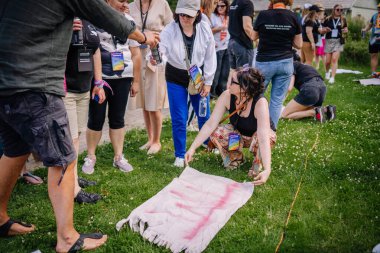 Sigulda, Letonya - 18 Temmuz 2025 - Bir hippi festivalindeki insanlar yaratıcı bir atölyeye katılıyorlar, çimlerin üzerindeki kumaşı boyamak için sprey boya kullanıyorlar, sanatsal ifadeleri bir araya getiriyorlar..