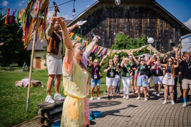 Sigulda, Letonya - 18 Temmuz 2025 - Neşeli bir grup açık hava hippi temalı bir etkinlikte renkli kurdeleler, müzik ve kırsal bir ahır yakınlarındaki güneşli gökyüzünün altında tezahürat yapan katılımcılarla kutlama yapıyor..