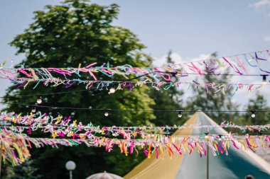 Renkli kurdeleler ve ip ışıkları büyük bir çadır, şemsiye ve hippi temalı süslemelerle güneşli bir açık havada asılı duruyor..