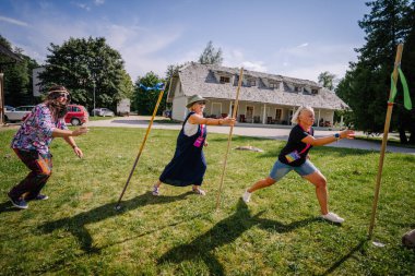 Sigulda, Letonya - 18 Temmuz 2025 - Katılımcılar eğlenceli bir takım aktivitesinde güneşli bir gökyüzünün altında çimlerin üzerinde coşkuyla koşan hippi temalı bir festival sırasında canlı bir açık hava bayrak yarışına katıldılar..