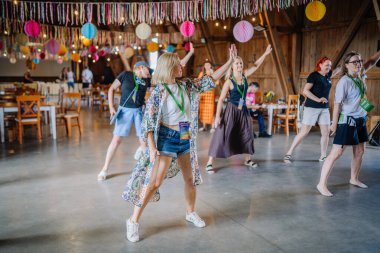 Sigulda, Letonya - 18 Temmuz 2025 - Bir grup kadın, renkli asılı dekorasyonlarla çevrili, neşeli bir atmosferde müzik, hareket ve cemaatin tadını çıkaran, kapalı bir hippi festivalinde dans ediyor..