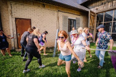 Sigulda, Letonya - 18 Temmuz 2025 - Aralarında hippi esinlenilmiş bireylerin de bulunduğu bir grup insan güneşli bir takım oluşturma etkinliği sırasında kırsal bir binanın yakınlarında eğlenceli bir açık hava su oyununa katılıyorlar..