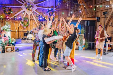 Sigulda, Letonya - 18 Temmuz 2025 Hippi temalı bir etkinlikte neşeli bir şekilde kutlama yapan bir grup insan renkli ışıklar, dekorasyonlar ve birlik ve heyecan içinde el kaldırdı..