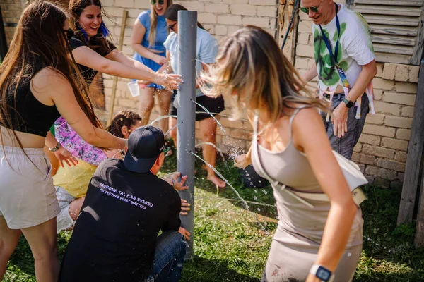 Sigulda, Letonya - 18 Temmuz 2025 - Hippi temalı bir açık hava etkinliğinde insanlar bir su borusu yarışmasında birlikte gülüyor ve çalışıyor, su sıçratıyor ve eğlenceli bir takım çalışması ve eğlencesinin tadını çıkarıyorlar..