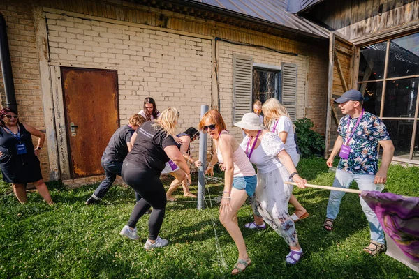 Sigulda, Letonya - 18 Temmuz 2025 - Aralarında hippi esinlenilmiş bireylerin de bulunduğu bir grup insan güneşli bir takım oluşturma etkinliği sırasında kırsal bir binanın yakınlarında eğlenceli bir açık hava su oyununa katılıyorlar..