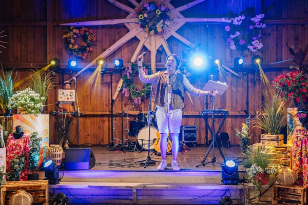 Sigulda, Letonya - 18 Temmuz 2025 - Müzik aletleri, çiçekler ve ışıklarla çevrili, dekore edilmiş bir sahnede hippi temalı bir etkinlik sunucusu. Renkli festival havası. Hippi..