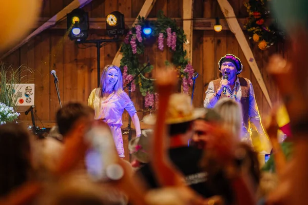 Sigulda, Letonya - 18 Temmuz 2025 - Hippie temalı göstericiler, renkli ışıklar, çiçekler ve şenlikli atmosferle donatılmış ahşap bir mekanda heyecanlı bir seyirciyle sahneye çıktılar.