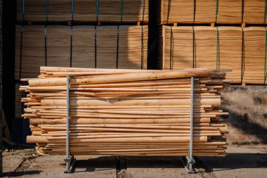 Valmiera, Letonya - 10 Eylül 2025 - Bir ahşap fabrikasının arka planında demet desenli kaplama çarşafları olan yuvarlak ahşap çubuklar veya direkler düzgünce bir metal çerçeveye yerleştirilmiş.