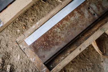 Ahşap çerçeveye monte edilmiş yıpranmış endüstriyel bir bıçağın yakın çekimi tozlu bir atölye zemininde yatıyor, pas, metal doku ve alet yapım detaylarını gösteriyor.