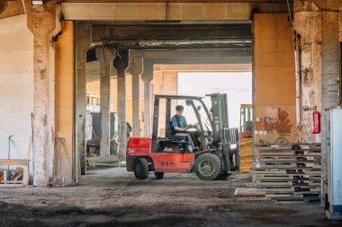 Valmiera, Letonya - 10 Eylül 2025 - Bir işçi, paletler, beton sütunlar ve inşaat malzemeleriyle dolu bir alanda sanayi deposu içinde kırmızı bir forklift kullanıyor..