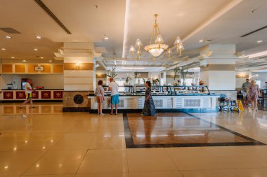 Kemer, Tureky - 18 Eylül 2025 - İnsanlar şık ışıklandırma, çiçekler ve temiz, modern bir iç mekan ile süslenmiş, açık bir otel büfe restoranında yemek seçiyorlar..