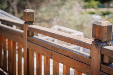 Güneş yanığı ahşap korkuluklara yakın çekim ve doğal, kırsal bir son. Arka plan hafifçe bulanık, ahşabın dokusunu ve detaylarını vurguluyor..