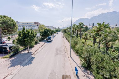 Kemer, Tureky - september 18, 2025 - Sunny street scene with parked cars, tourist buses, palm trees, hotel buildings, and a mountain range in the background, viewed from a pedestrian bridge.