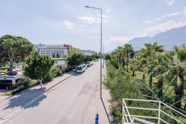 Kemer, Tureky - september 18, 2025 - Sunny street scene with parked cars, tourist buses, palm trees, hotel buildings, and a mountain range in the background, viewed from a pedestrian bridge.
