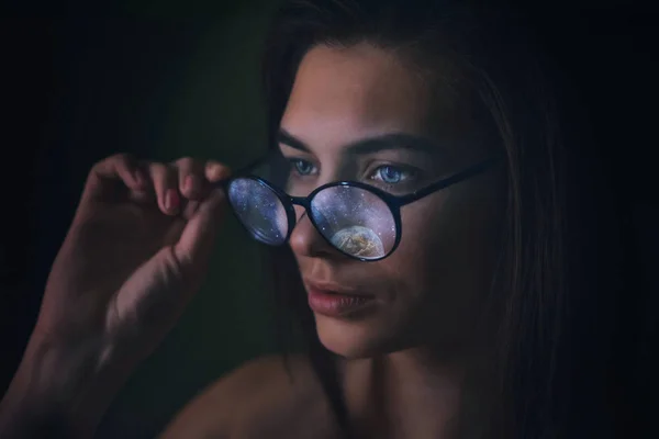 Girl in glasses with the reflection of cosmic stars of the planets, portrait of a woman advertising optics. Unusual Magic Eyeglass Lens